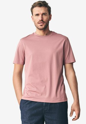 Camiseta de manga corta y cuello redondo en algodón de color rosa claro. Presenta una textura suave y un corte relajado, combinada con vaqueros de mezclilla oscura.