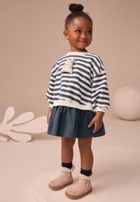 Stribet bomuldssweatshirt i marineblå og hvid med en bjørneaccent. Kombination med et marineblåt skørt og beige ankelstøvler med pelskant.