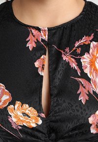 Černý květinový top s oranžovými a růžovými květy, s malým vykrojením u výstřihu a jemným texturovaným vzorem.