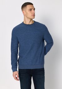 Jersey azul de hombre fabricado en punto texturizado, con mangas largas y cuello redondo. Combina con vaqueros oscuros para un look casual.