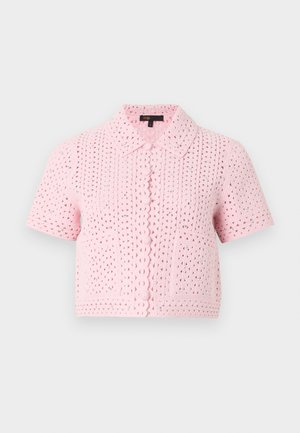 Kvinde iført en pink kortærmet crop top med hulmønster, hvid top nedenunder, blå viddeben jeans med små mønstre og sorte sko med hæl.