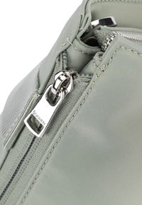 Angolo di borsa in nylon verde chiaro con zipper argento e linguetta di estrazione. Presenta un tessuto testurizzato e dettagli cuciti visibili.