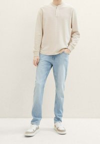 Beige gestreiftes Langarm-Henley-Shirt, hellblaue gerade geschnittene Jeans und weiße Sneaker mit beigen Akzenten. Lässige Kleidung für den Alltag.