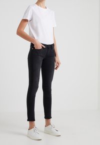 Camiseta de algodón blanca, vaqueros skinny negros, deportivas blancas casuales. Diseño simple sin patrones; el corte ajustado acentúa la silueta.