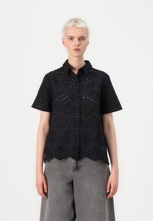 Blouse noire à manches courtes avec des motifs en œillets complexes, un ourlet festonné et un devant à boutons. Fabriquée en tissu léger.