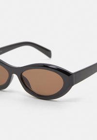 Ochelari de soare negri cu un design retro în formă de inimă, având lentile ovale maronii și cadre din plastic neted. Lățimea lentilelor este ușor mai mare în centru.