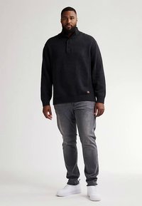 Donker gebreide trui met een kraag en drie knopen, gecombineerd met lichtgrijze jeans en witte sneakers. Gladde textuur, losse pasvorm.