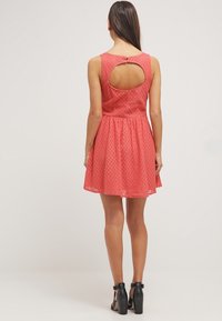 Robe corail avec une jupe évasée, un tissu texturé, un design sans manches et un détail découpé dans le dos. Associée à des talons noirs à bride à la cheville.