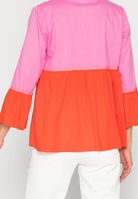 Top color-block con una sezione superiore rosa e una sezione inferiore arancione a campana, dotato di maniche a 3/4. Realizzato in tessuto leggero.