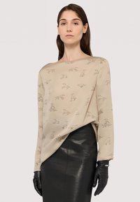 Beżowa bluzka z abstrakcyjnym szarym nadrukiem psa, luźny krój, szeroki dekolt typu łódka oraz długie rękawy, w połączeniu z czarną skórzaną spódnicą i rękawiczkami.