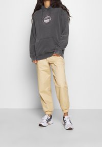 Grå huvtröja med en globgrafik, tillsammans med ljusbeiga tapered joggerbyxor och vita sneakers med svarta accenter.