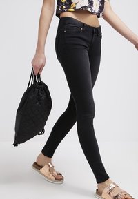 Svarta skinny jeans med hög midja, kombinerat med en blommig croptop och svart dragkedjepåse. Sandalerna har ett rem i roséguld.