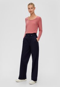 Langärmliges pinkes Oberteil mit Rundhalsausschnitt, kombiniert mit hoch geschnittenen marineblauen Hosen mit doppelt knopflosem Verschluss und seitlichen Taschen.