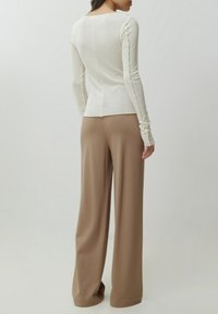Lange mouwen, off-white top met een gestructureerde afwerking. Gepaard met hoge taille, wijdvallende beige broeken van een gladde stof.