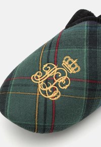 Green plaid slipper featuring a thick textile upper with red and yellow accents, and an embroidered gold logo design with a crown.