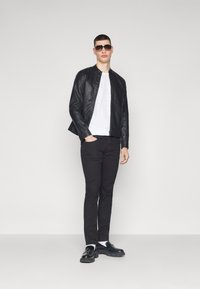 Chaqueta de cuero negra con cierre de cremallera sobre una camiseta blanca, combinada con pantalones negros y zapatos negros gruesos. Los accesorios incluyen gafas de sol.