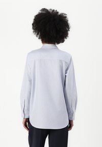 Modra in bela črtasta srajca z dolgimi rokavi in ovratnikom. Mehka tkanina z gumbnimi manšetami. Zaobljen rob in sproščen kroj.