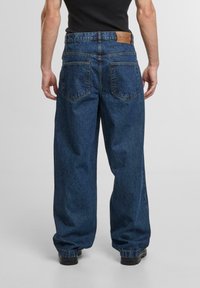Blauwe denim wijde jeans met een leren taillebandpatch en twee achterzakken. De stof heeft een klassieke, gestructureerde afwerking.