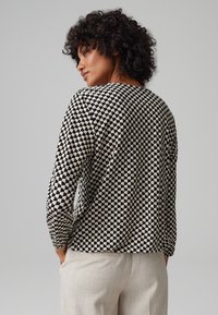 Langärmliges Oberteil in Schwarz und Creme mit geometrischem Muster, mit rundem Halsausschnitt und lockerer Passform, sowie leicht gerafften Ärmeln.