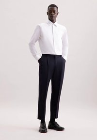 Weißes Hemd mit Knöpfen, kombiniert mit marineblauen plissierten Hosen und schwarzen Anzugschuhen. Glatter Stoff, maßgeschneiderte Passform und klassisches Design.