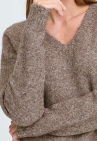 Brown knitted sweater with a V-neck; soft, textured fabric with a slightly fuzzy finish. Long, fitted sleeves and a relaxed fit.