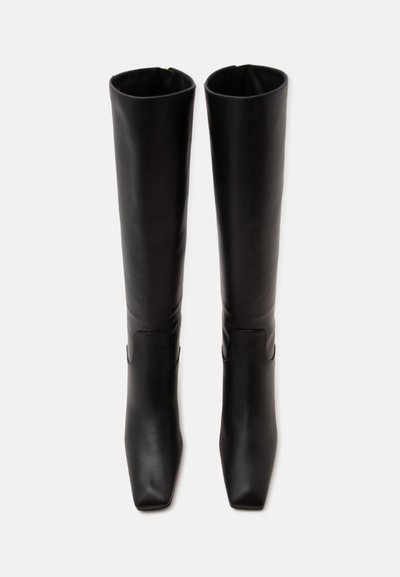 Paire de bottes hautes en cuir noir à bouts carrés vues de face sur fond blanc.