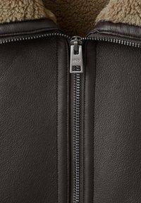 Giacca di pelle marrone scuro con colletto in shearling, dotata di una zip argento e finitura texture. Cuciture dettagliate sono visibili lungo le cuciture.