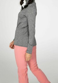 Maglietta grigia a maniche lunghe con collo alto, realizzata in tessuto testurizzato, abbinata a pantaloni aderenti rosa chiaro con tasche laterali.