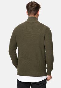 Suéter de punto acanalado verde oliva con un cuello alto, mangas largas y una silueta ajustada. Tejido texturizado con un diseño simple.