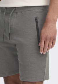 Shorts en coton gris avec une poche latérale zippée, un cordon de serrage ajustable et une texture lisse. L'ourlet est fini par une simple couture.