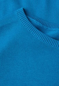 Blau gestrickter Stoff mit einer glatten Textur. Verfügt über einen Rundhalsausschnitt mit einem gerippten Rand. Nahaufnahme, die die gleichmäßige Farbe und das Muster hervorhebt.