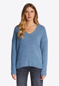 Blauw gebreid sweater met een V-hals, ribbelstructuur, lange mouwen en een licht gebogen zoom. Gecombineerd met donkergrijze jeans.