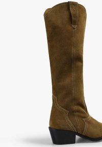 Bota de ante marrón hasta la rodilla con un tacón cuadrado, que presenta costuras decorativas y un diseño de costura curvada.