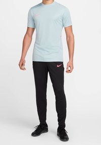 Camiseta deportiva de manga corta azul claro con logo Nike rosa, combinada con pantalones deportivos negros con el swoosh de Nike en rosa, enfatizados por un ajuste ceñido.