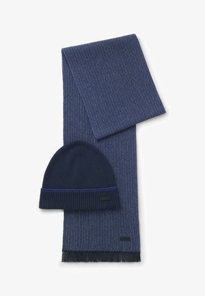 Marine strikksjal med frynser og en matchende hue. Begge har en ribbet tekstur og et subtilt mønster med en kontrasterende blå stripe.