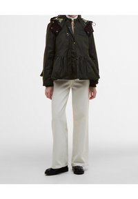 Groene doorgestikte jas met peplumtaille, ribfluwelen schouderstukken en gouden ritsen. Gecombineerd met crèmekleurige wijde broekspijpen en zwarte laarzen.