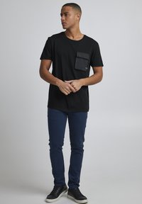 Černé bavlněné tričko s přední kapsou, v kombinaci se štíhlými tmavomodrými kalhotami a černými teniskami s bílou podrážkou. Jednoduchý design.