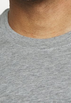 Nek en onderkaak van een persoon die een lichtgrijs shirt met ronde hals draagt, met zichtbare huidstructuur en korte haarstoppels.