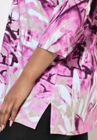 Lyhythihainen ylisuuri paita valkoisena, jossa on vaaleanpunainen ja ruskea abstrakti kuosi. Sivuhalkiot ja rento istuvuus, valmistettu kevyestä kankaasta.