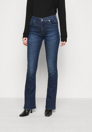 Jean en denim bleu foncé évasé avec une taille mi-haute, design à cinq poches et décoloration subtile. Associé à des escarpins noirs à bout pointu.