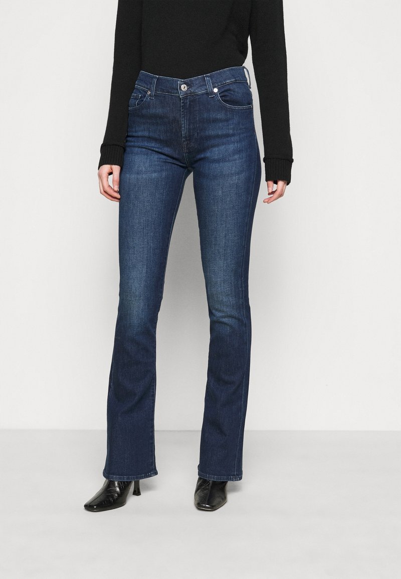 Jean en denim bleu foncé évasé avec une taille mi-haute, design à cinq poches et décoloration subtile. Associé à des escarpins noirs à bout pointu.