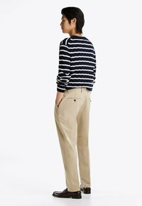 Gestreifter navyblauer und weißer Pullover mit ribbeliger Textur, kombiniert mit hellbeigen Hosen. Abgerundet mit dunkelbraunen Schuhen, von der Seite betrachtet.