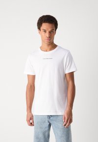 White cotton T-shirt with short sleeves, crew neckline, featuring “Calvin Klein Jeans” logo printed in black at the chest.