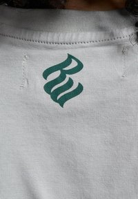 Lys grå t-skjorte stoff med en ribbet tekstur. Har en grønn, stilisert logo trykket på baksiden nær halsen.