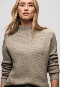 Pull en maille côtelée beige avec un col montant, présentant des motifs texturés diagonaux et des poignets retroussés. Tissu léger.