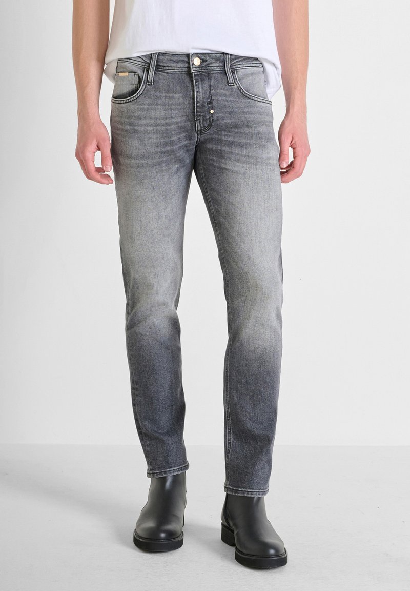 Jeans en denim gris délavé avec une coupe slim, un design à cinq poches, un léger effet de décoloration et des accents en métal argenté, associés à des bottines noires.