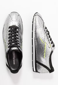 Sneaker metallici argento con un motivo a pelle di serpente testurizzat, lacci neri, interni neri e dettagli gialli. Suola in gomma con striscia bianca.