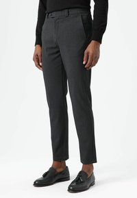 Dunkelgraue, maßgeschneiderte Hosen mit schlanker Passform, glatter Textur, vorderen Falten und Seitentaschen, kombiniert mit schwarzen Slippern.