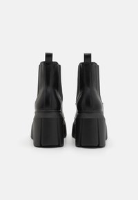 Stivali alla caviglia in pelle nera con suola platform spessa. Presentano una texture liscia, linguette per facilitare l'indossamento e dettagli con cuciture verticali.