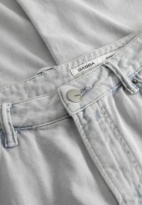 Ceinture de jeans en denim gris clair avec bouton visible et étiquette de marque "GABBA" sur un fond en tissu assorti.